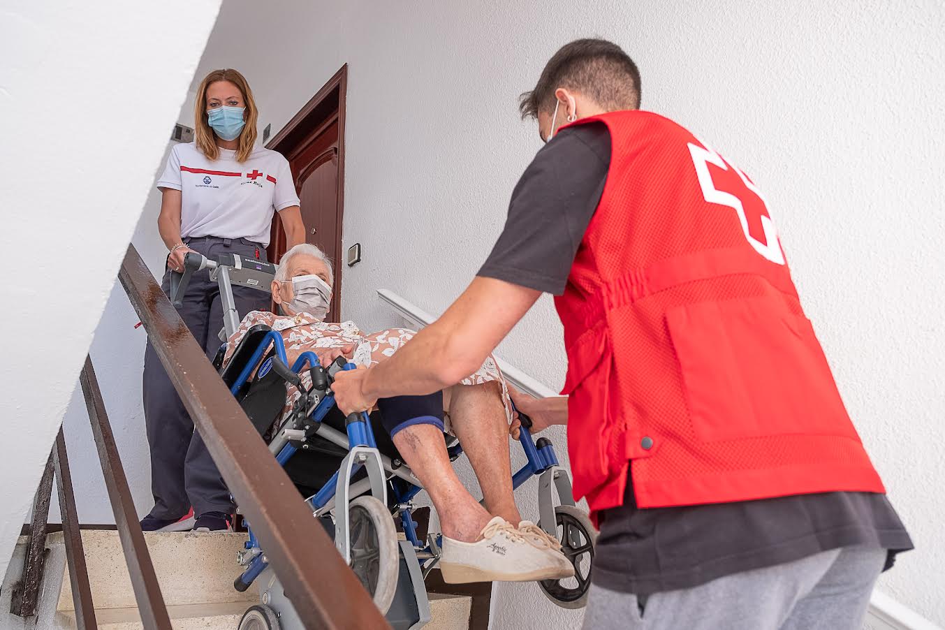 Personal de la Cruz Roja ayuda a una señora a bajar las escaleras de su casa.