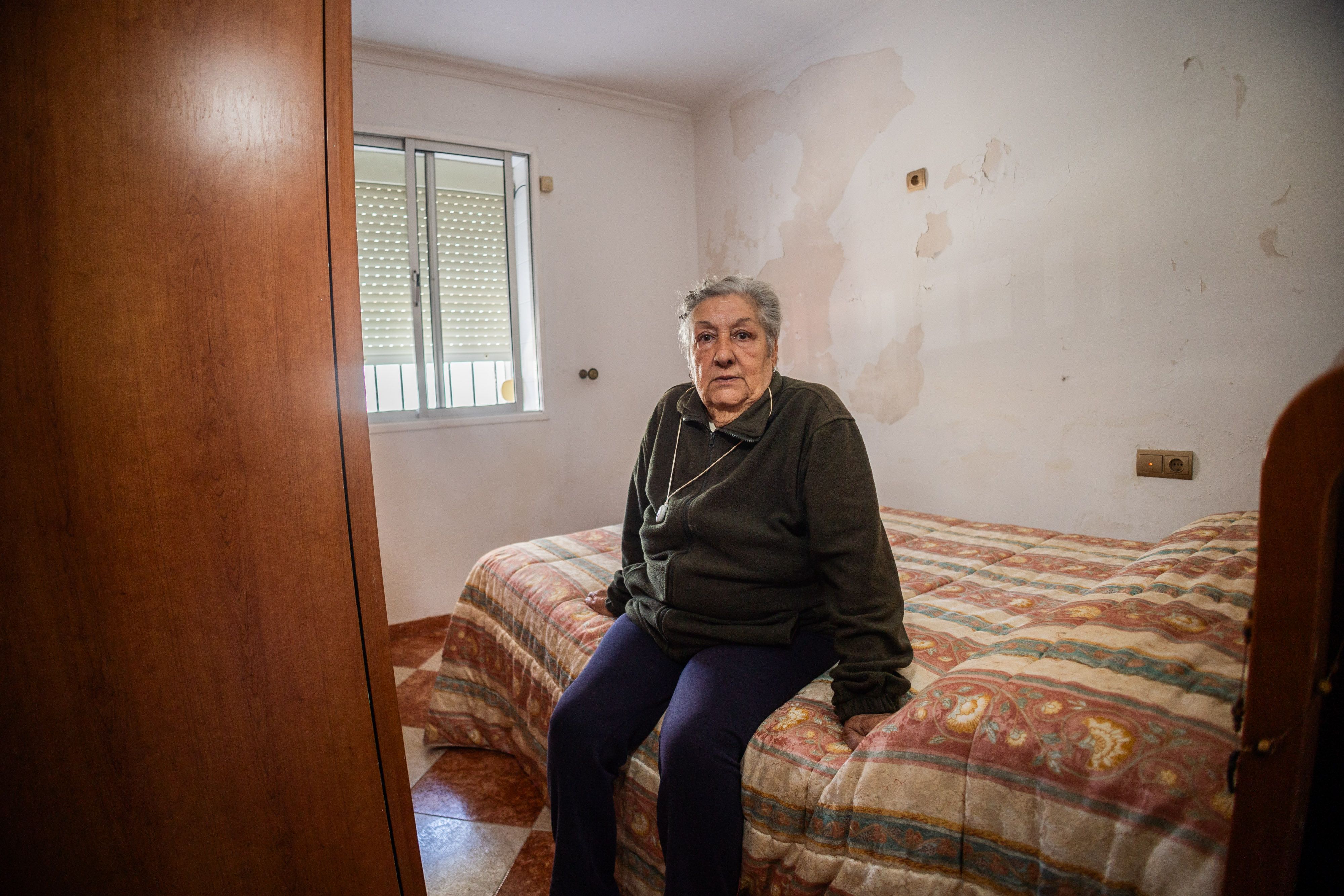 María Josefa Moreno, vecina de La Asunción, sentada en su cama, tras la cual se pueden apreciar las humedades que aparecieron, según señala, a raíz de las obras.