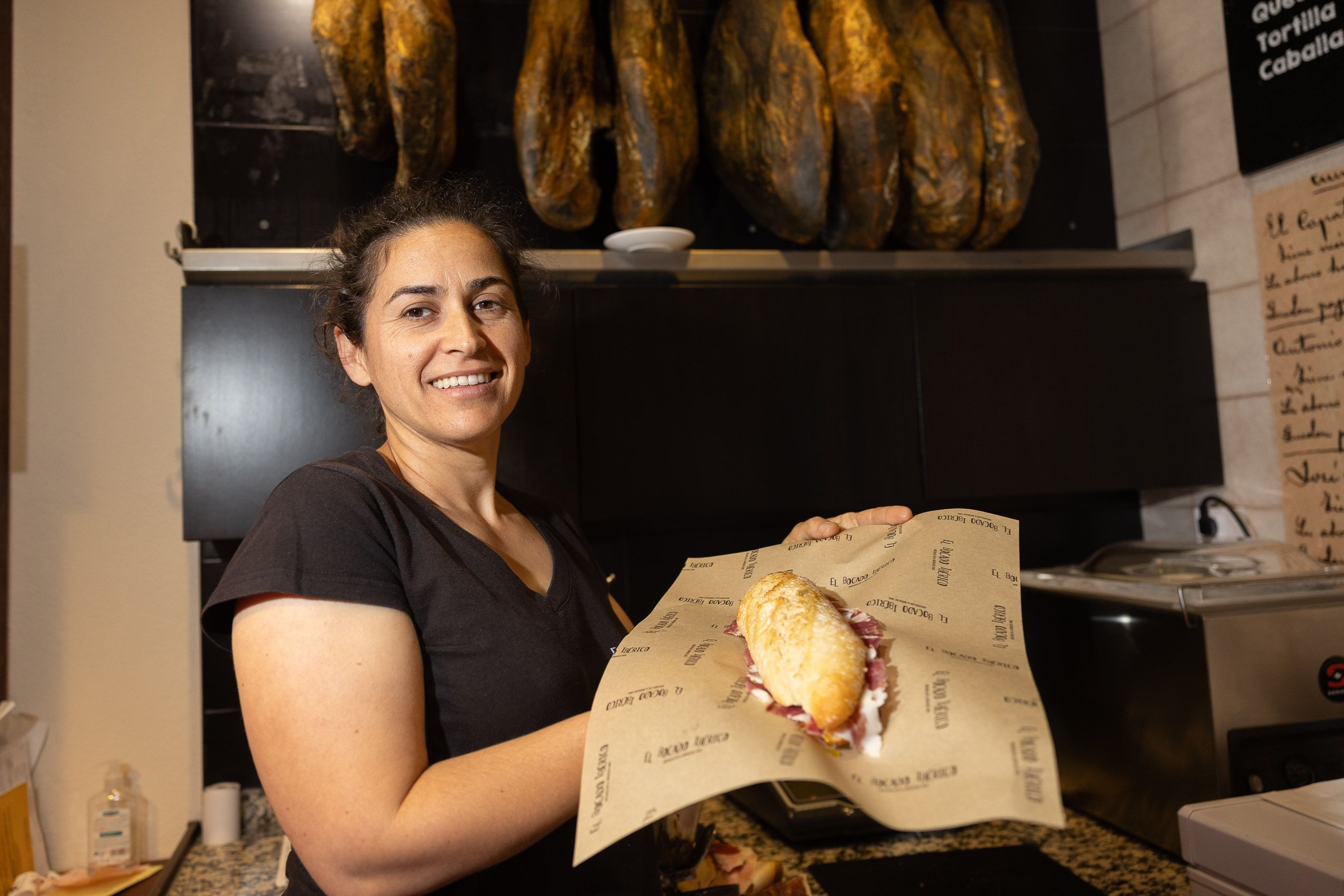 Ana Álvarez en la tienda con un bocadillo de jamón de los que vende en sus manos. 
