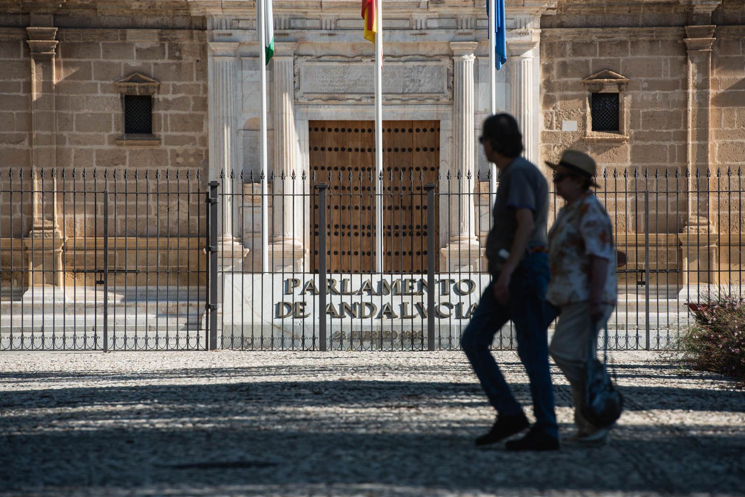 Dos personas pasean por delante del Parlamento de Andalucía.