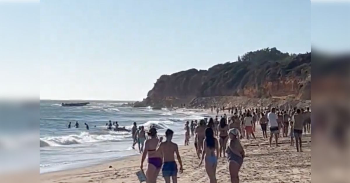 Bañistas, en La Barrosa, con la narcolancha al fondo en el agua.