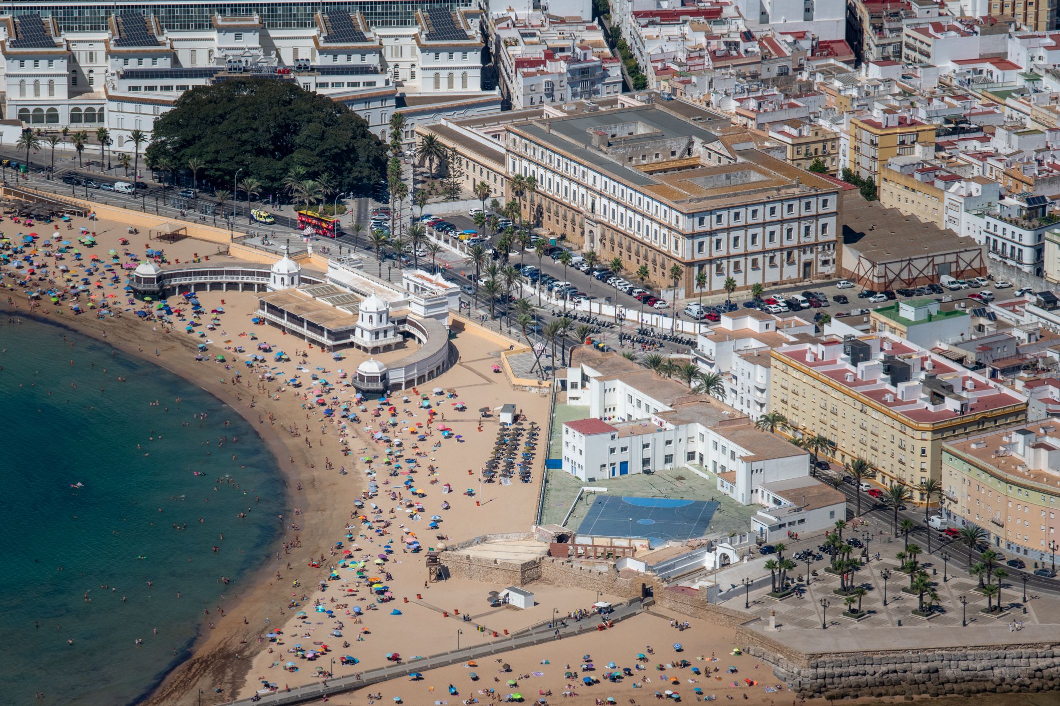 Vista aérea del Balneario de La Palma, sobre la arena de la playa de La Caleta, y del colegio Santa Teresa, con pista deportiva de color azul.