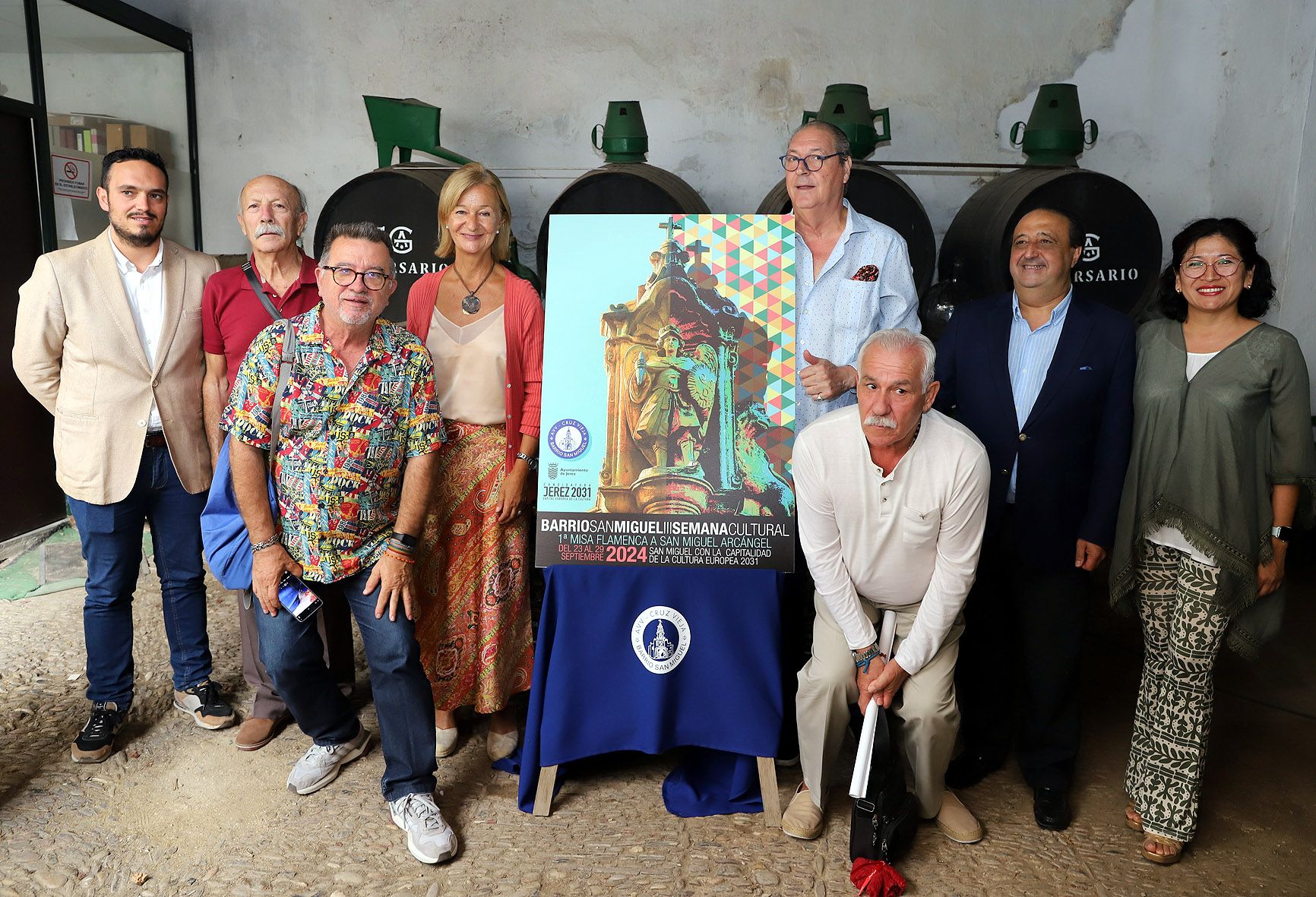 El presidente de la asociación del barrio, vecinos y delegados junto al cartel de la semana cultural.