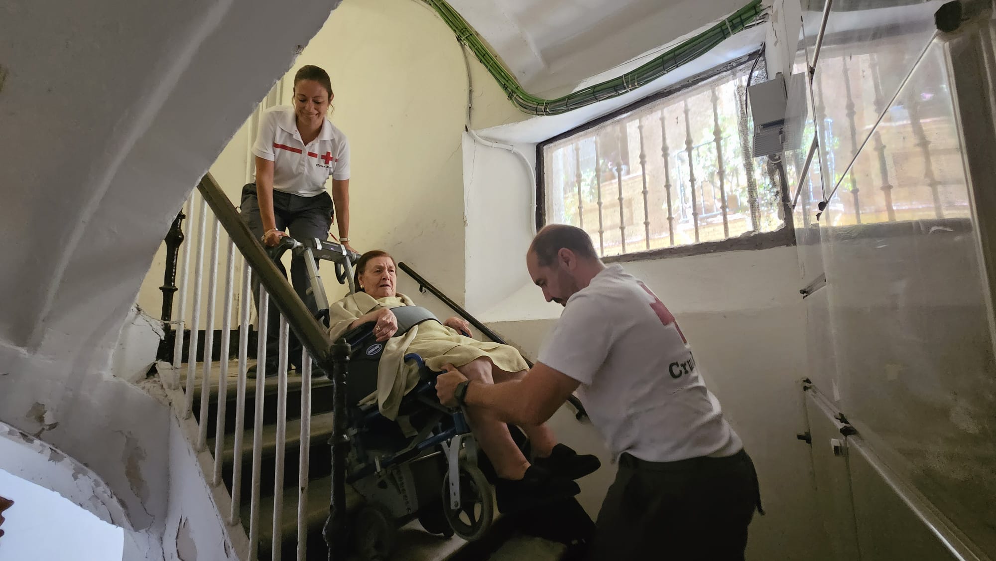 Manuela es ayudada por los operarios de Cruz Roja a bajar desde su casa.