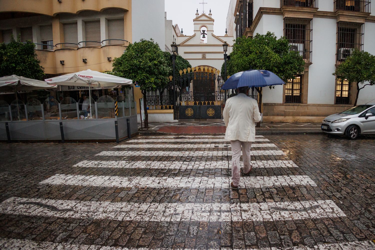 Una persona con paraguas cruza un paseo de peatones en la Alameda Cristina de Jerez.