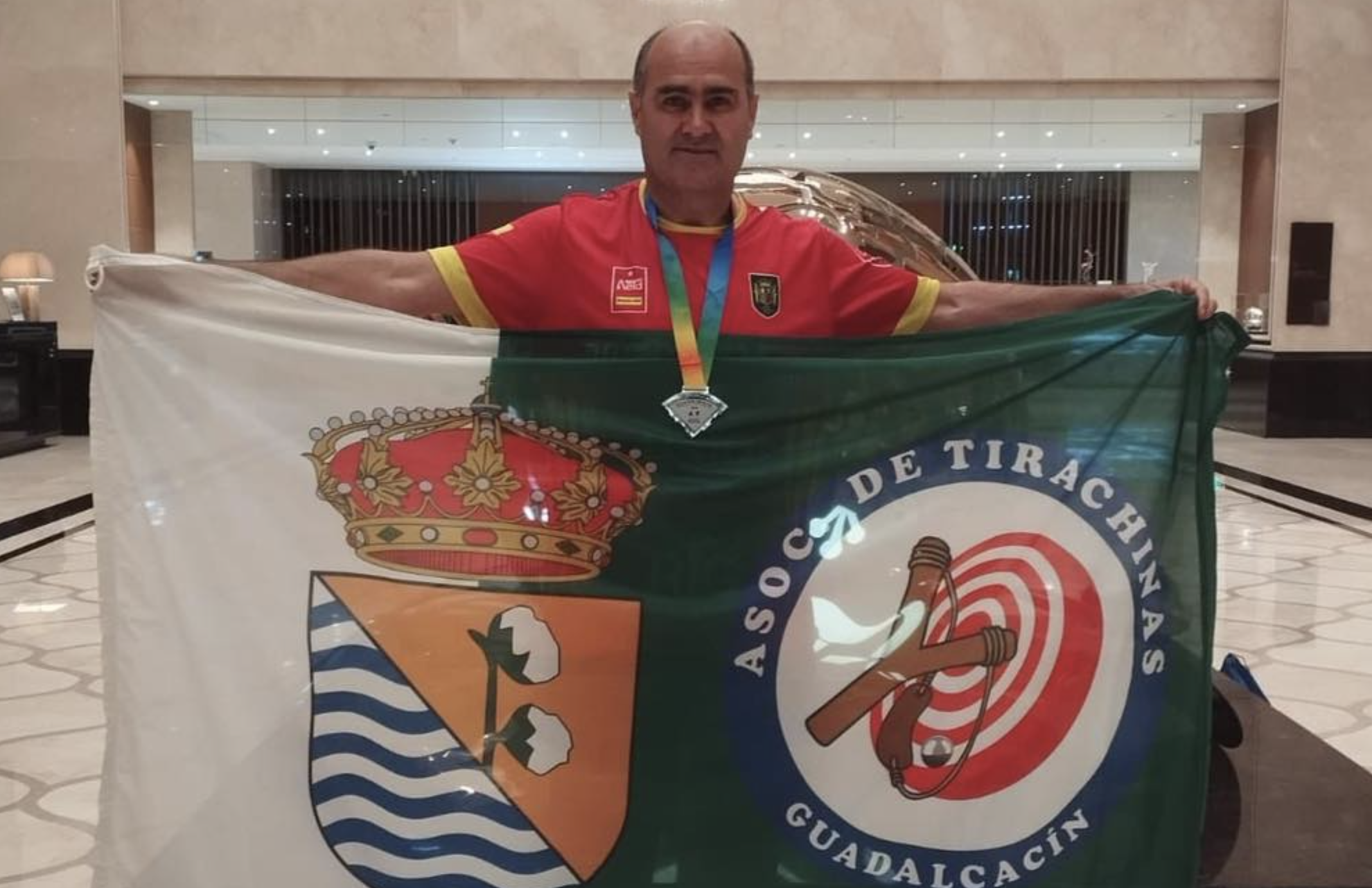 José Vela, en China, con una bandera con el escudo de Guadalcacín y de la Asociación de Tirachinas de esta ELA de Jerez.