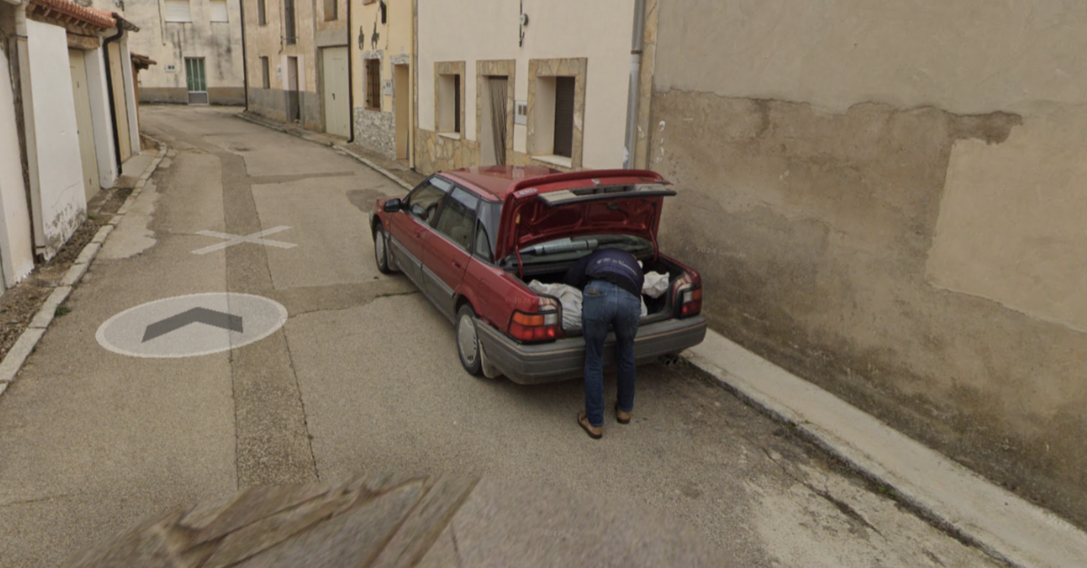 Un hombre, introduciendo un cadáver en el maletero de su coche. 